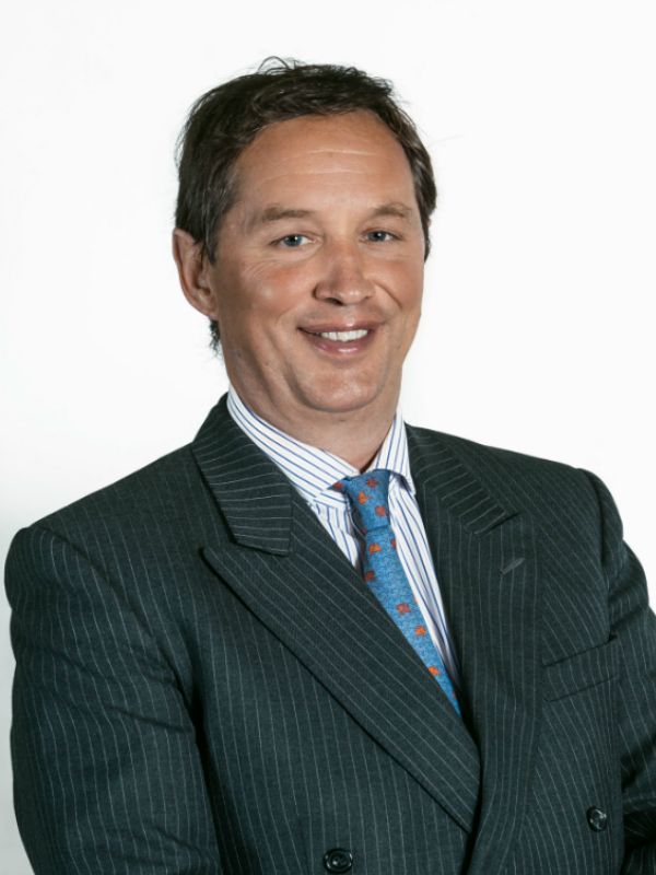 Jeremy Findlay sits side on, smiling at the camera. He is wearing a grey pinstripe suite, a blue and white striped shirt and a blue tie.