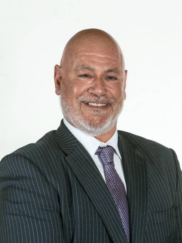 Tom Trotter smiles at the camera. He is wearing a grey pinstripe suit jacket, a white shirt and a dark coloured tie.