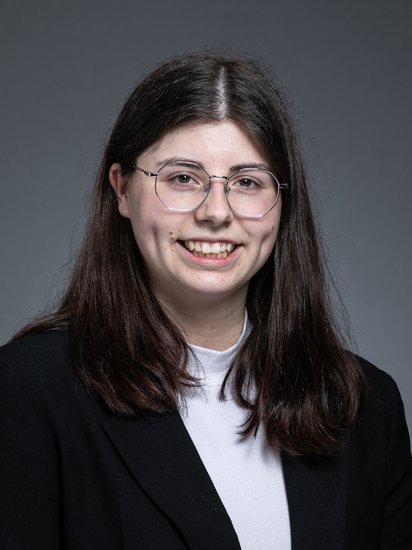 Brooke Ritchie smiles at the camera. She is wearing a black jacket and white blouse and has glasses on.