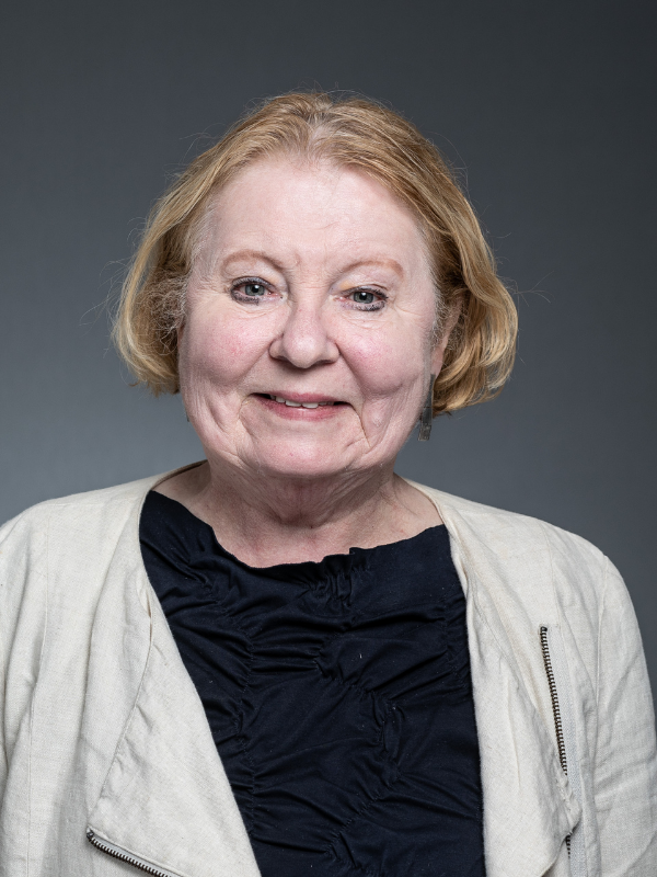 Carol McFarlane faces the camera smiling. She is wearing a beige blazer and black blouse.