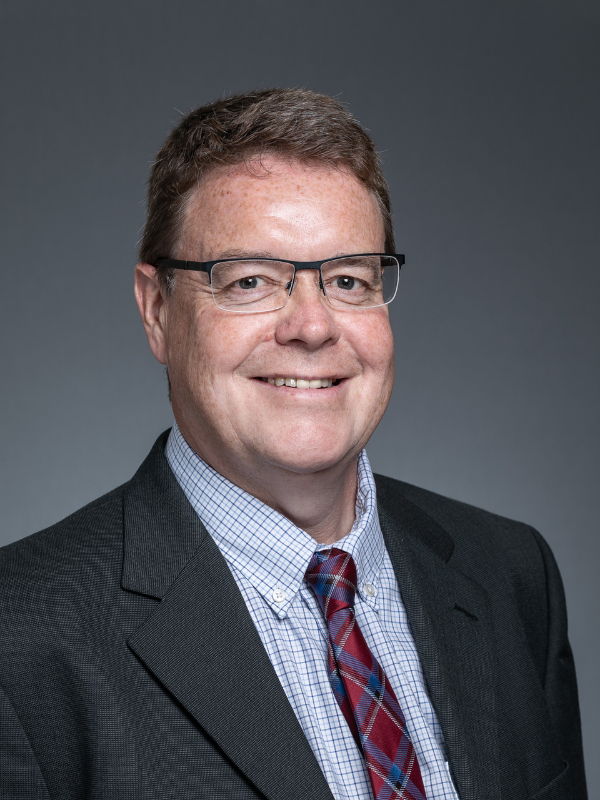 Colin Yorkston smiles at the camera. He wear glasses and a dark suit jacket, a blue striped shirt and a red patterned tie.
