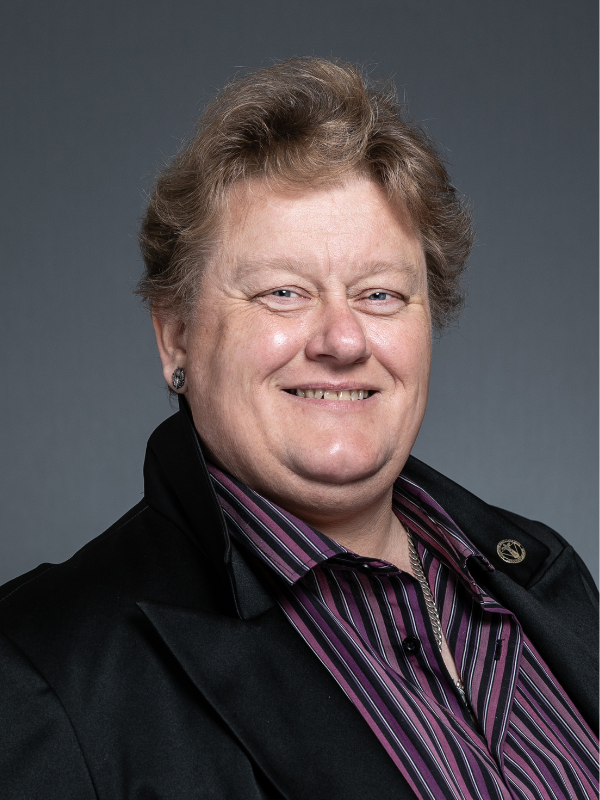 Councillor Donna Collins sits side on to the camera, smiling at it. She is wearing a black jacket and purple and black striped shirt.