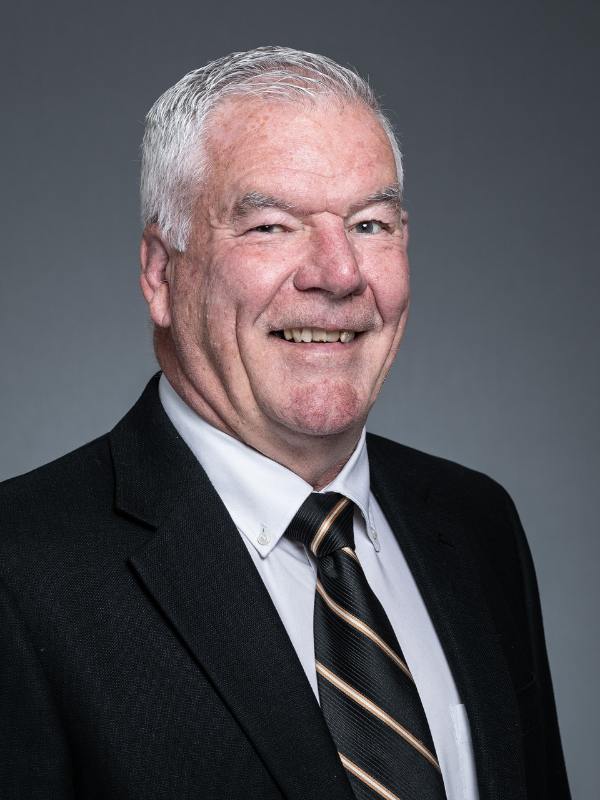 George McGuire smiles at the camera, wearing a black suit jacket, a white shirt and black and gold striped tie.
