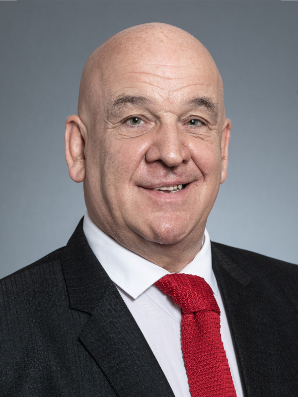 Norman Hampsire smiles at the camera. He is wearing a black suit jacket, white shirt and red tie.
