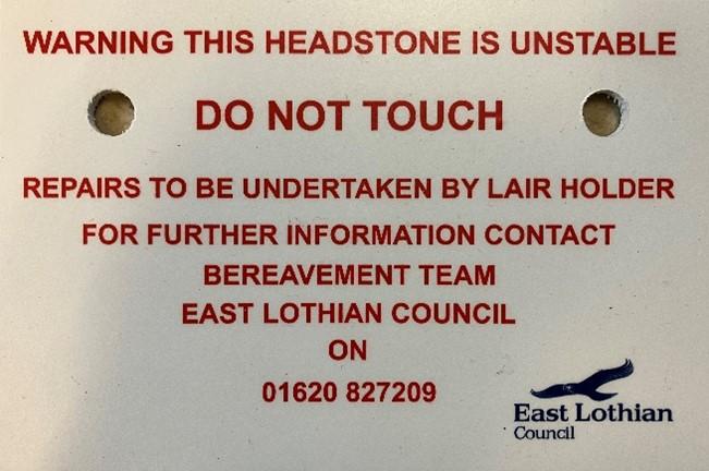 Headstone warning sign that says: Warning this headstone id unstable. Repairs to be undertaken by lair holder, For further information contact the Bereavement Team.