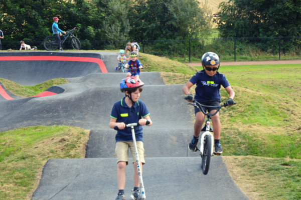 Children on scooters and bikes going round a pump track.