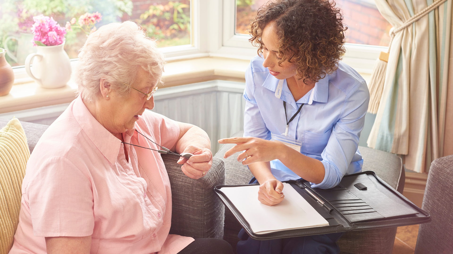 older lady is being shown how to use an alarm pendant