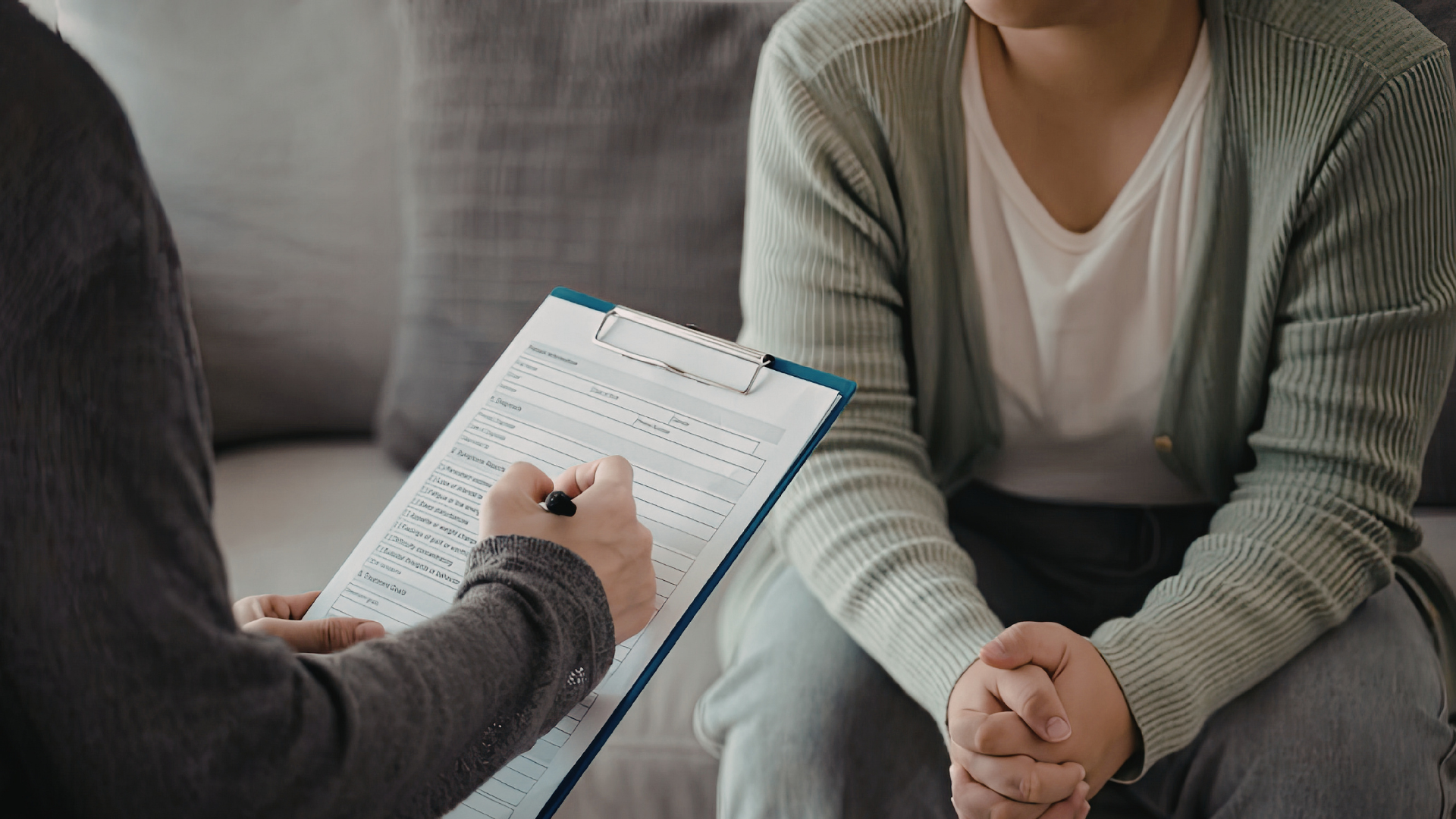 Two people chatting during a counselling session.  One person is holding a clipboard writing notes