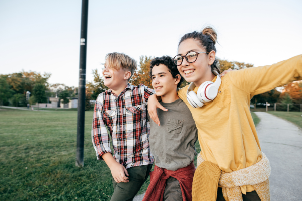 Three young people, arms around each other, walking and laughing.