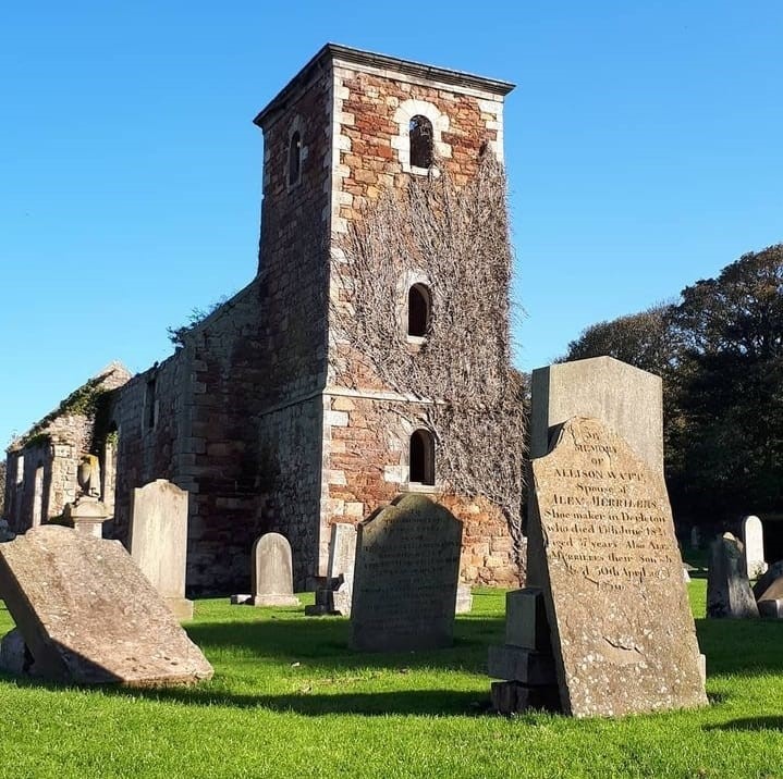 A historic church building in a graveyard against blue skies