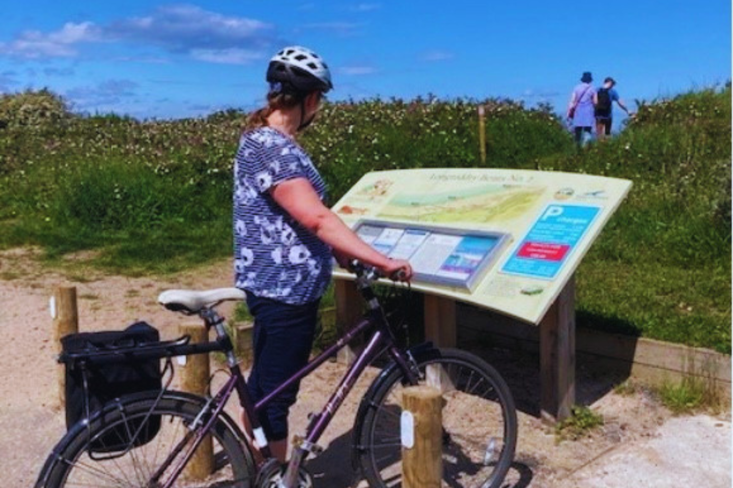 A cyclist in the countryside reading an information board.