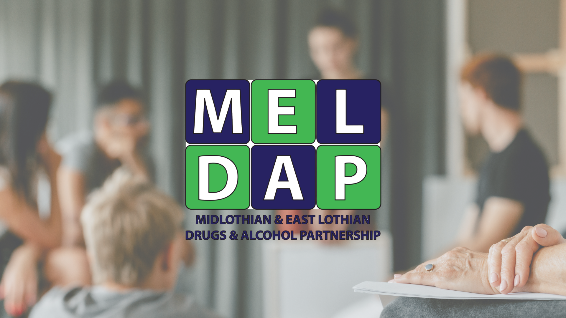 Background shows a group discussion, foreground features MELDAP logo 