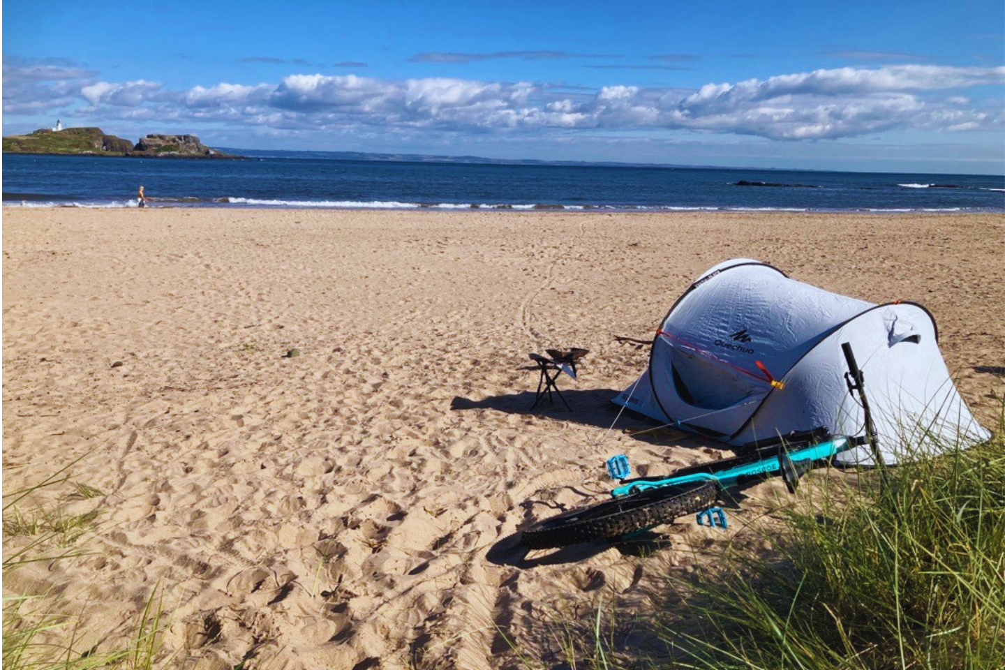 A tent pitched by a sand dune with a bicycle next to it.