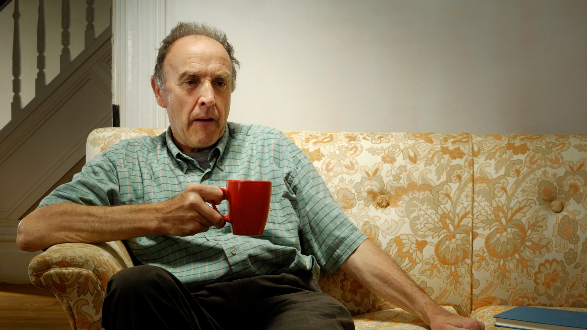 man sitting on a sofa alone with a cup of coffee