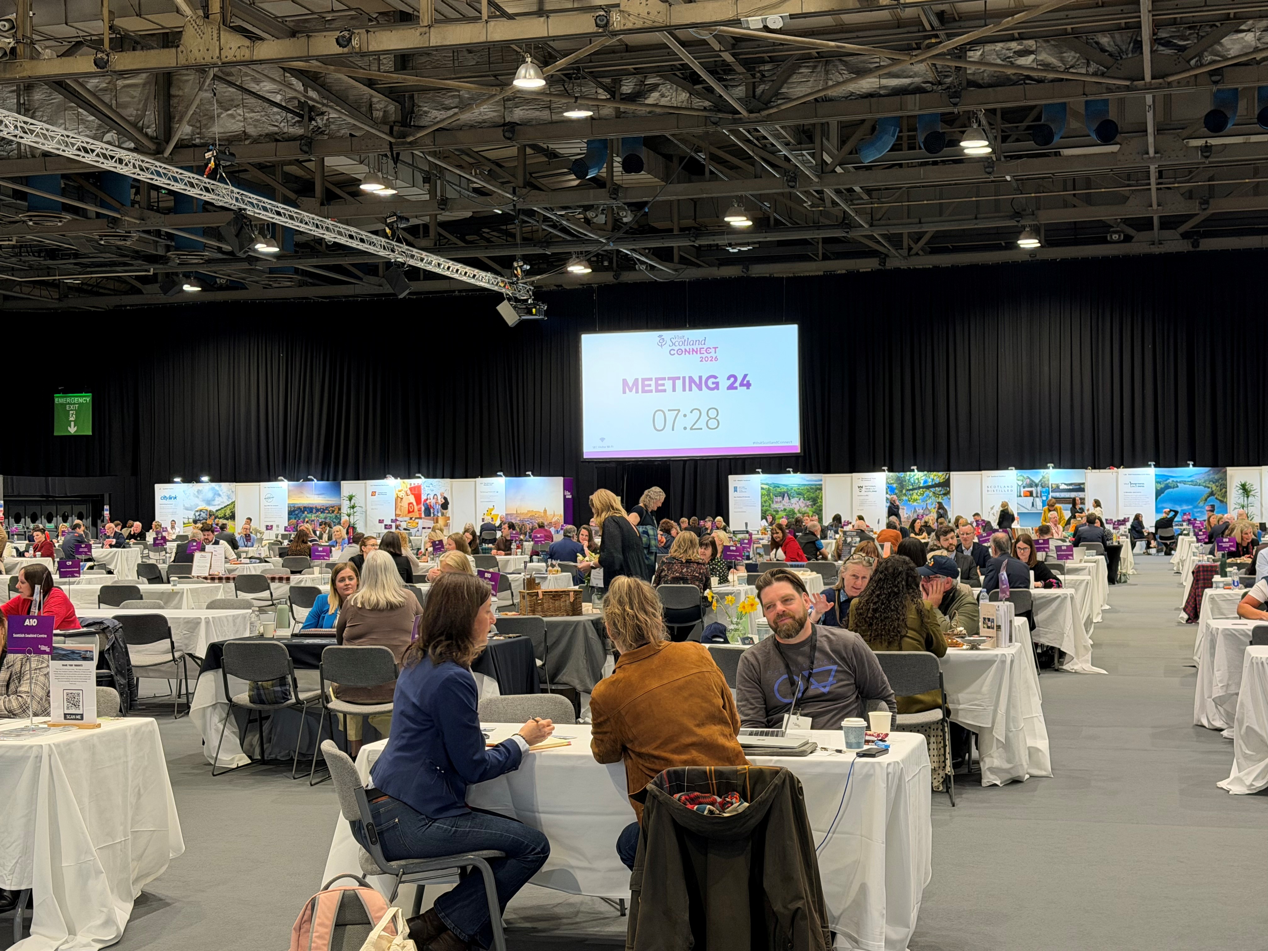 Photo of groups of people talking at tables in a large exhibition hall