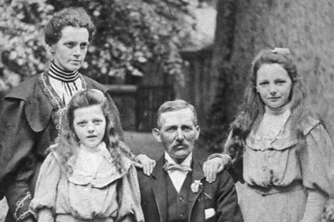 John Gray is photographed with his wife and two daughters. They sit in the foreground with his wife standing behind.