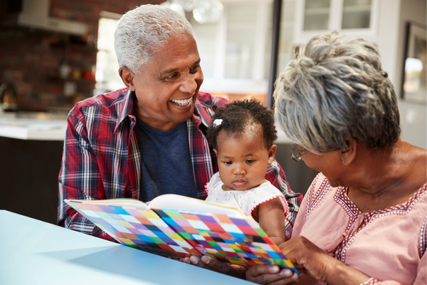 Image of grandparents smiling while reading a book to a young toddler