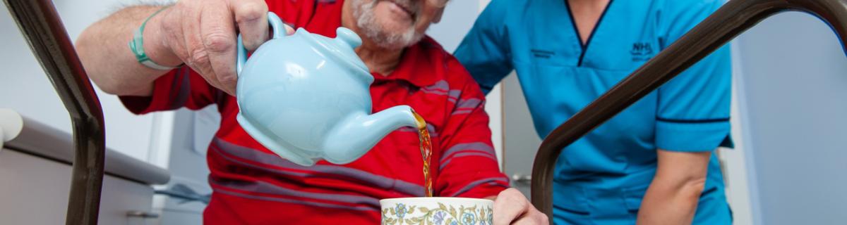 Older man is pouring a cup of tea with cup on an assistance trolley