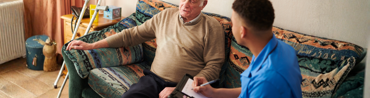older man sitting on sofa speaking to a care assistant