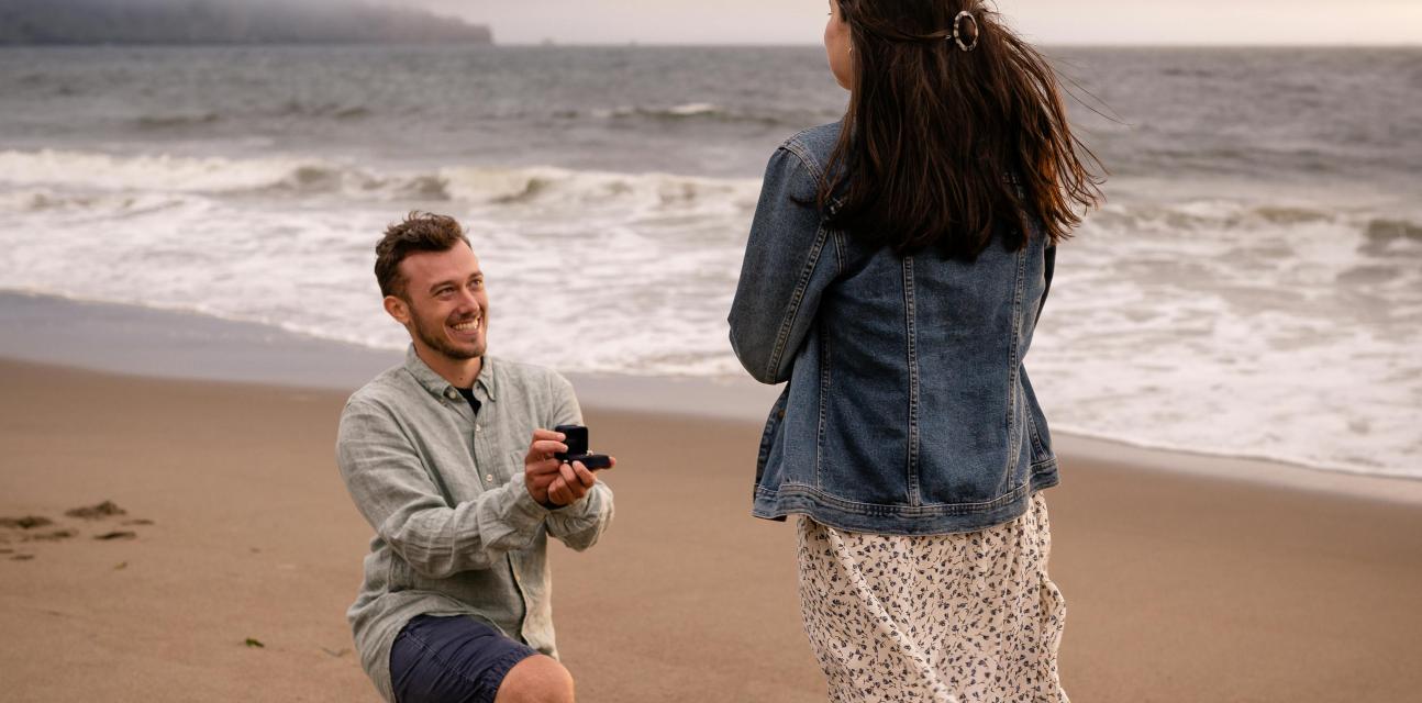Wedding proposal on a sandy beach with the sea in the background.